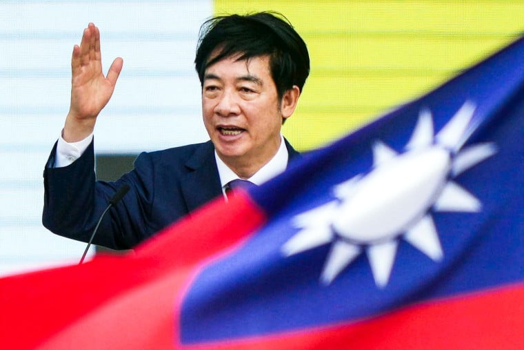 Lai Ching-te speaks at a podium, with a hand up, and the Taiwan flag flying in the foreground