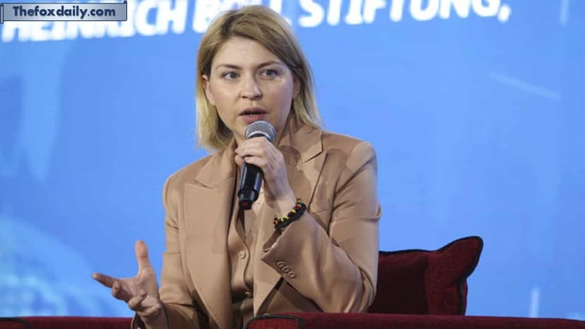 Olha Stefanishyna holding and speaking into a microphone whilst seated against a blue background during a speaking engagement
