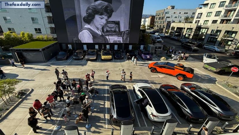 People wait in line as Tesla electric vehicles, including the Cybertruck, park beneath a giant movie screen at the Tesla Diner
