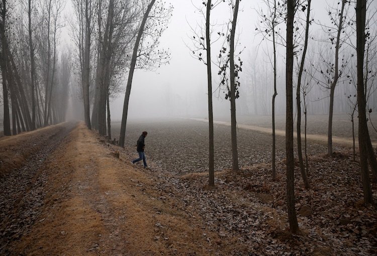 A man crosses a dried water canal amid fog in Pulwama district, Kashmir.