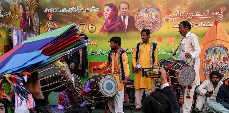 Artists play traditional drums next to a hoarding with portraits of Pakistan