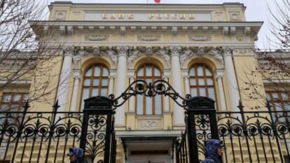 Two guards in blue camouflage uniforms stand outside the Russian Central Bank building with white columns and decorative gates Two guards in blue camouflage uniforms stand outside the Russian Central Bank building with white columns and decorative gates