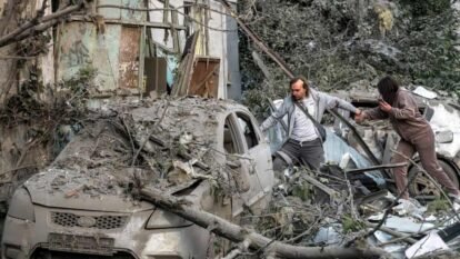 Two people climb over debris and damaged cars near a destroyed building in Kyiv