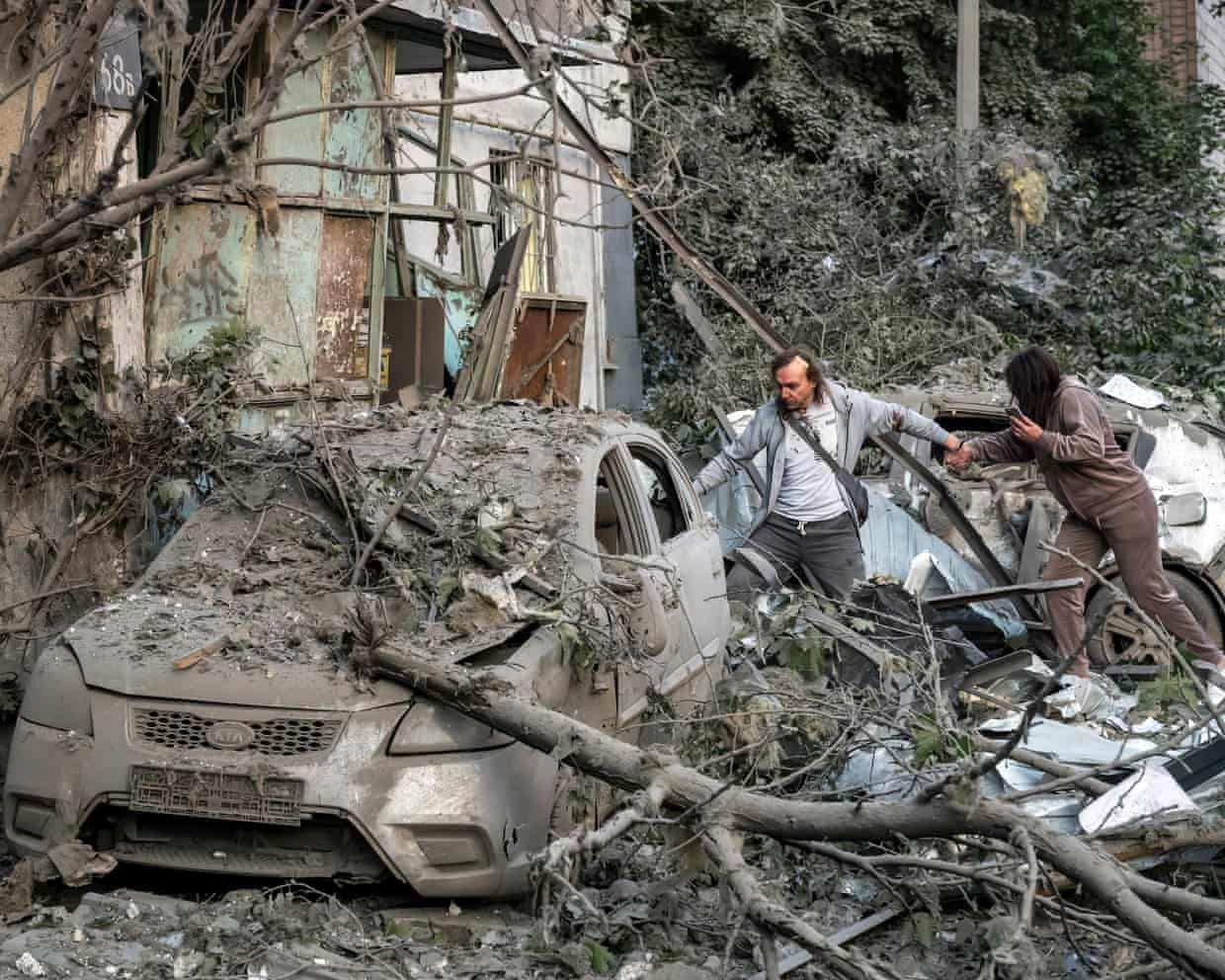 Two people climb over debris and damaged cars near a destroyed building in Kyiv