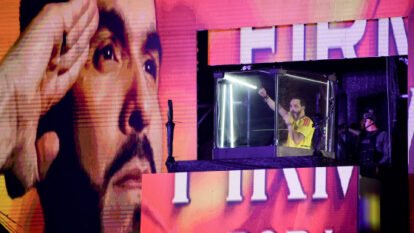 Abelardo de la Espriella raises a fist into the air while speaking into a microphone from inside an elevated, bulletproof glass cube.