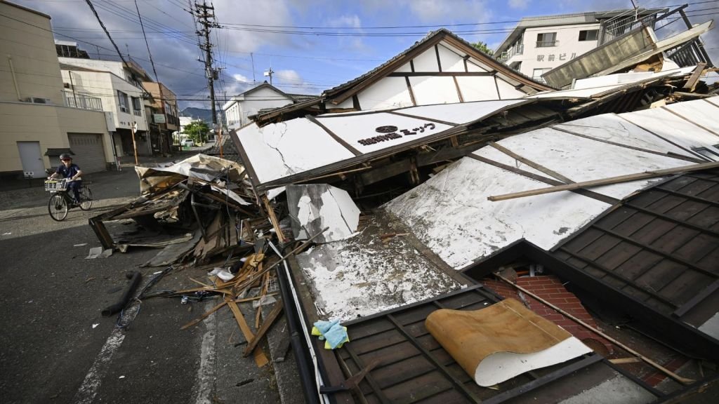 Person on a bike passes by collapsed houses, a day after an earthquake in Yatsushiro, Kumamoto prefecture