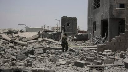 A soldier inspects rubble in the street.